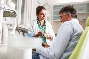 Smiling dentist showing patient model of teeth