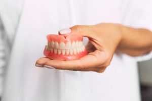 a dentist holding a set of full dentures in their left hand